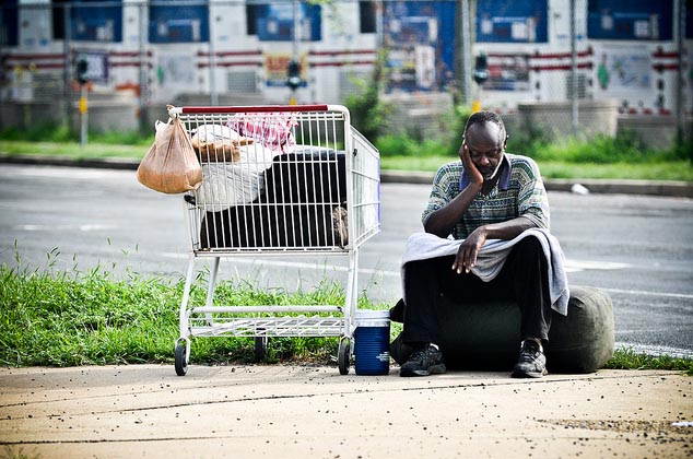 Homeless man sits with shopping cart