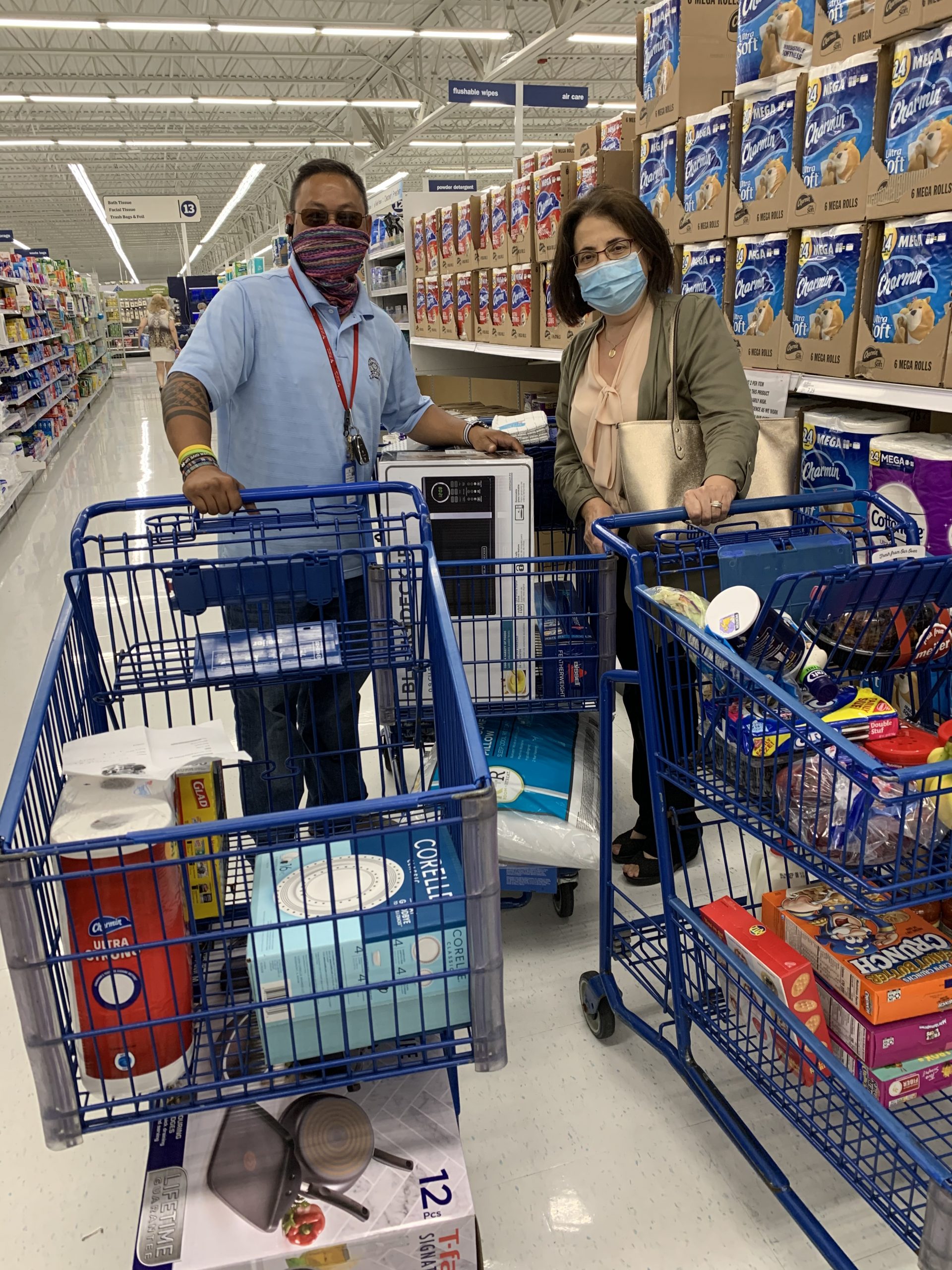 Two people with masks on and shopping carts full of supplies in a supermarket.