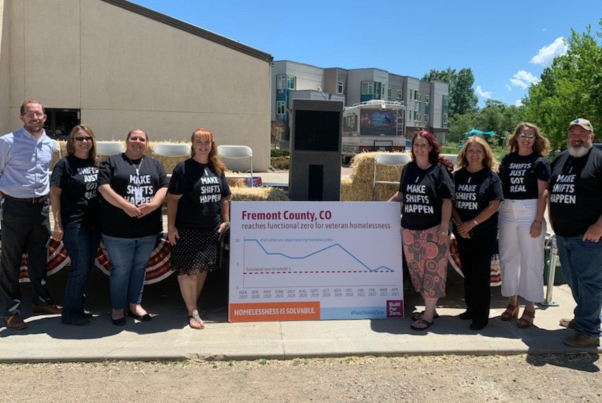 The team in Fremont County, CO holds a functional zero data chart for veteran homelessness outside under the bright sun.