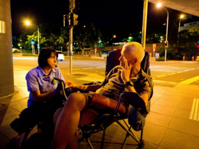 Woman kneeling talking to a man sitting in a chair at night underneath an overpass outside