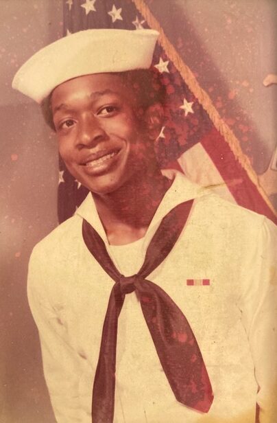 Older photograph of young Black teenager smiling wearing white Navy uniform with tie and hat
