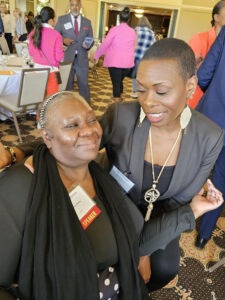 Two Black women side hugging at a conference.