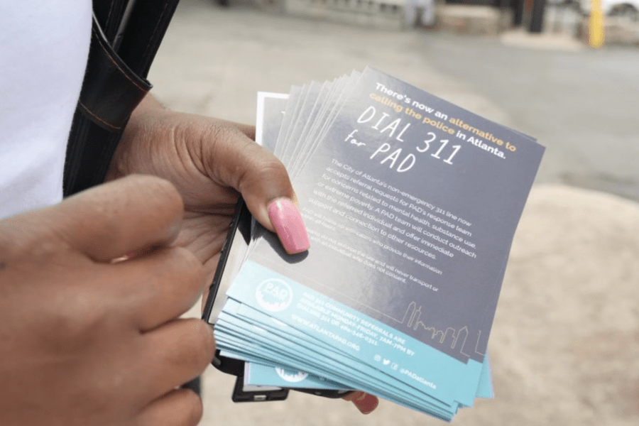 Image of a hand holding small flyers saying "There's now an alternative to calling the police in Atlanta. Dial 311 for PAD."